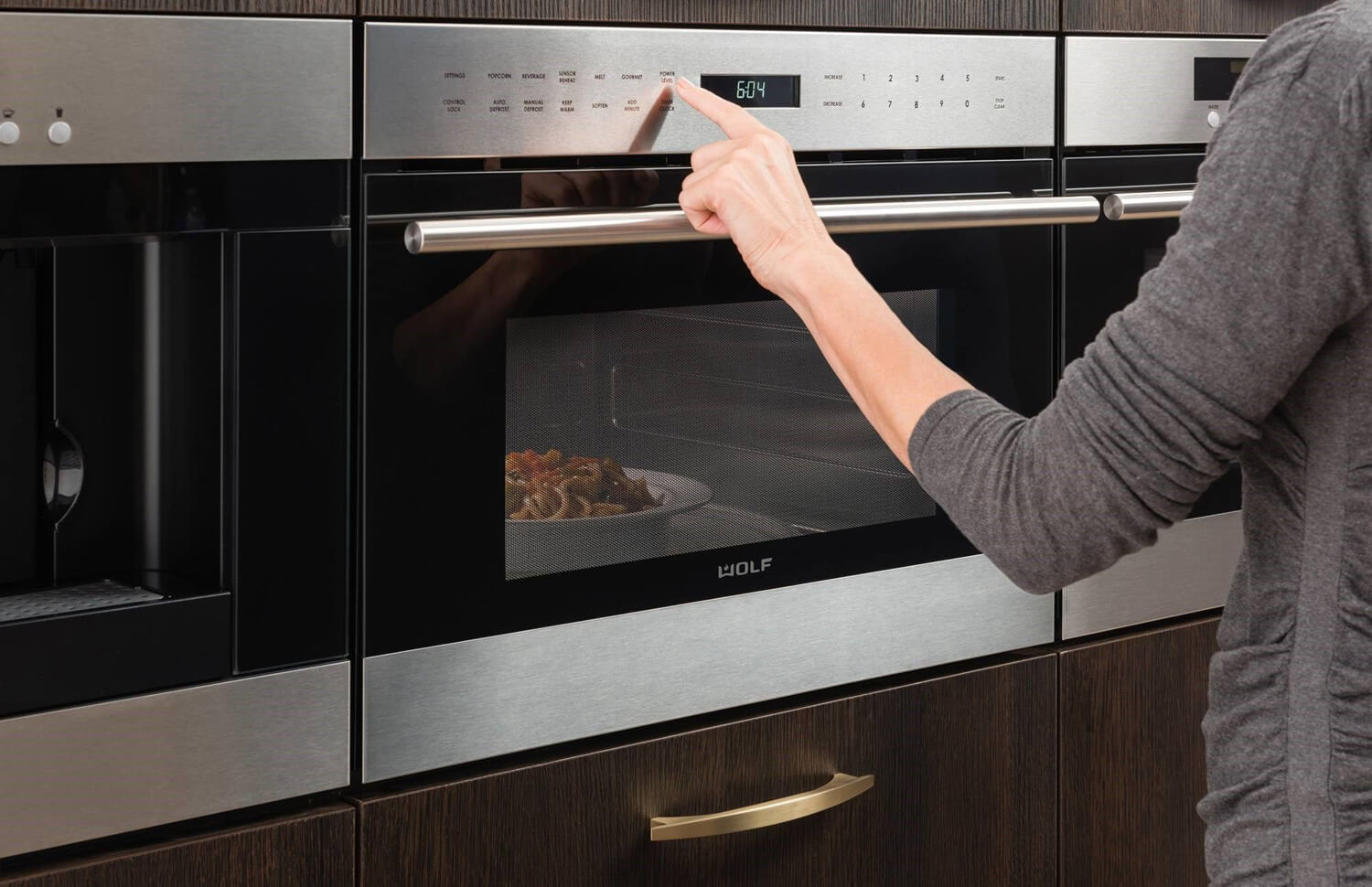 A woman pressing a button on a Wolf built-in microwave